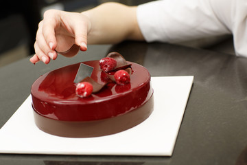 Close up of beautiful sweet cake put on white plate. Hand of professional confectioner decorating cake with chocolate. Concept of confectionery, sweet-shop and gastronomy.