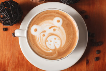 Cappuccino coffee with latte art in the form of bear close-up on a wooden table. The concept of coffee in the cafe