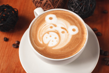 Cappuccino coffee with latte art in the form of bear close-up on a wooden table. The concept of coffee in the cafe