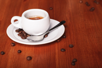 White espresso coffee Cup closeup, roasted coffee beans on wooden background. Concept of coffee break and serving coffee