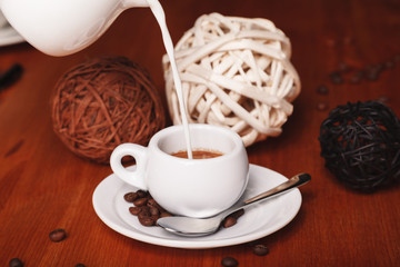 Pour milk from the milk jug into a Cup of espresso on a wooden background. Concept of coffee break and serving coffee