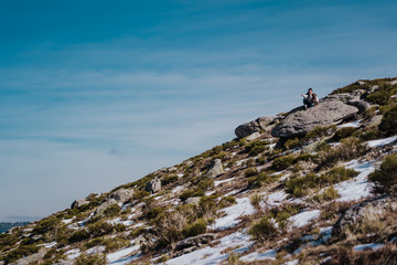 Young backpacker enjoying a sunny winter day in the mountains. Breathing fresh air, relaxed and carefree. Some snow all around. Amazing view. Lifestyle.