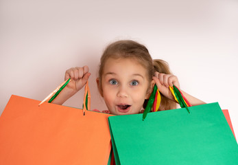 Shopping little girl holding shopping bags looking up to the side on ligth background at copy space..