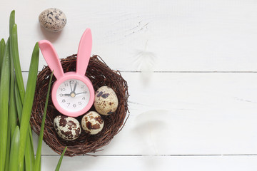 Pink bunny alarm clock and quail eggs in the nest on the white table. Eater top view card