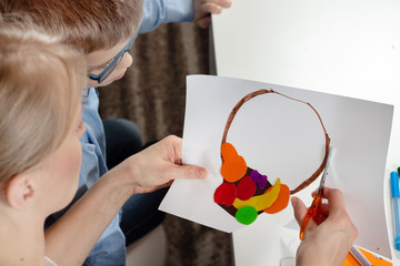 Chłopiec w niebieskiej koszuli z mamą. Mama chłopca wycina nożyczkami pracę plastyczną wykonaną przez dziecko. © Tomasz