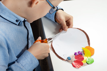 Praca plastyczna wykonywana przez dziecko. Chłopiec wycina nożyczkami do papieru.