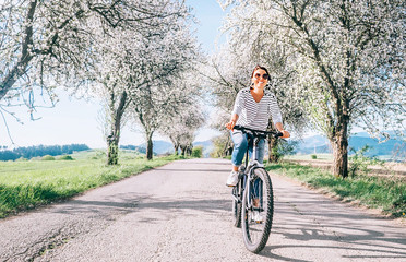 Happy smiling woman rides a bicycle on the country road under blossom trees. Spring is comming...