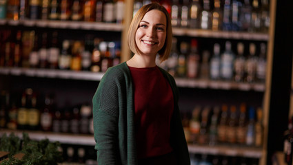 Photo of happy woman on blurred background of shelves with bottles of wine