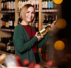 Image of happy woman with bottle in her hands on blurred background of shelves with bottles of wine