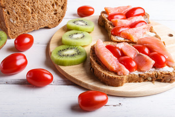 Smoked salmon sandwiches with butter and cherry tomatoes on white wooden background.