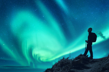 Aurora borealis and silhouette of a woman with backpack at night. Girl on the hill, starry sky with...