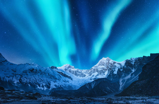 Aurora borealis above the snow covered mountain range in europe. Northern lights in winter. Night landscape with green polar lights and snowy mountains. Starry sky with aurora over the rocks. Space