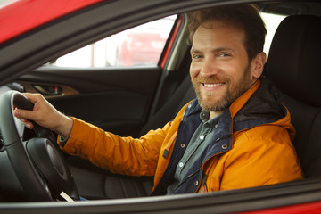 Side view of happy man sitting inside vehicle, smiling and looking at camera. Male customer testing...