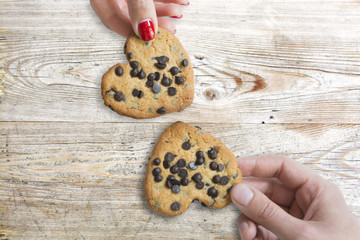 Young couple holding chocolate cookies in shape of hearts against wooden table, as love symbol 