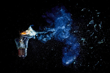 Сosmic explosion of burning light bulb with flying splinters of broken glass and smoke on isolate black background. Сoncept of creative art of starry sky, cosmos,  universe and the big bang theory. - obrazy, fototapety, plakaty