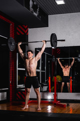 Fototapeta premium Sporty brutal strong guy doing exercises with a barbell in the gym. Brutal sports man. Bodybuilder in training in the gym. Health and fitness