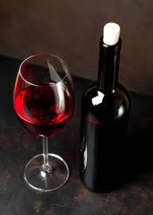 Wine glass with red wine and bottle against a stone background.