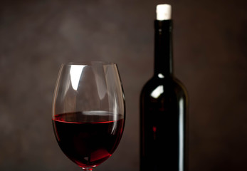Wine glass with red wine and bottle against a stone background.