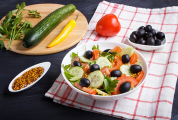 Vegetarian salad of tomatoes, cucumbers, parsley, olives and mustard on linen tablecloth.