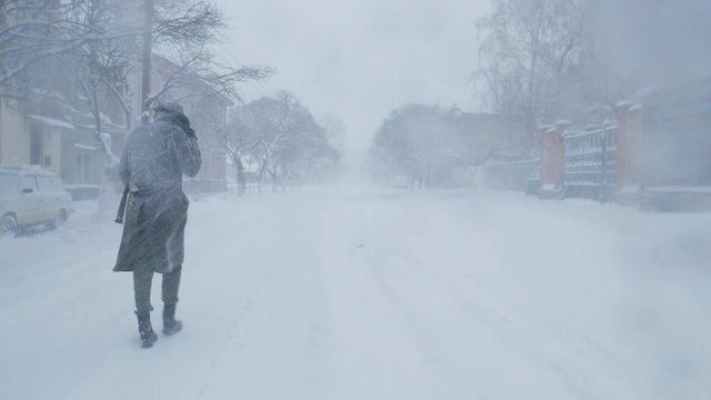Lonely man in coat and hat walks at the street during snow storm 