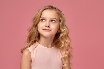 Little girl with a blond curly hair, in a pink dress is posing for the camera