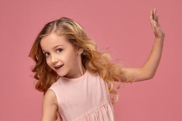 Little girl with a blond curly hair, in a pink dress is posing for the camera