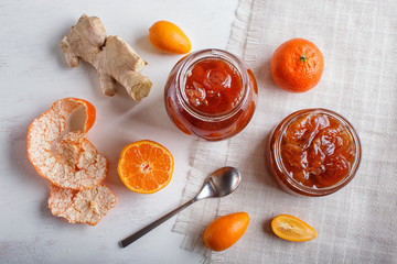 Tangerine and kumquat jam in a glass jar on white wooden  background.