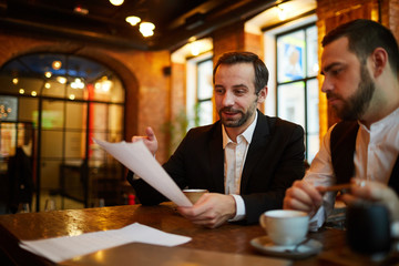 Portrait of two successful business people working in cafe discussing documents, copy space