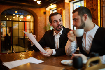 Portrait of two successful business people working in cafe discussing documents at coffee break, copy space
