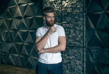 Perfect man. Young hipster holding hand on chin and looking at camera while standing against modern...