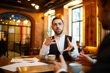 Portrait of successful businessman talking to partner during meeting in cafe and gesturing actively, copy space