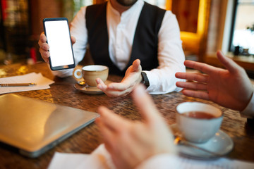 Closeup of successful businessman showing smartphone with blank screen during meeting in cafe, copy space