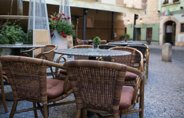 Empty rattan chairs and tables outside a street cafe at the city