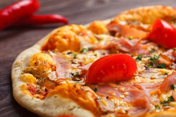 Close up top view Italian pizza with melted mozzarella cheese, red cherry tomatoes, ham and fresh green herbs on a brown table decorated by mushrooms, red sweet pepper and cherry tomatoes