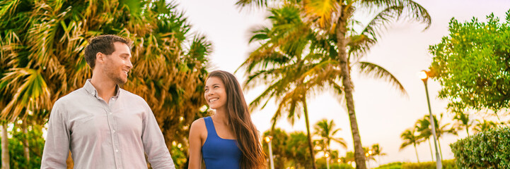 Happy couple young people lifestyle walking outside enjoying city night out at sunset on tropical beach background. Interracial relationship banner panorama.