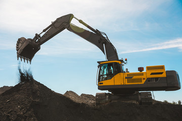 Yellow big excavator in the coal mine, loads the breed, with the bright sun and nice blue sky in...