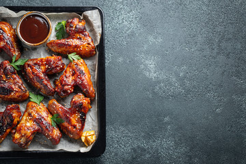 Roasted chicken wings in barbecue sauce with sesame seeds and parsley in a baking tray on a dark...