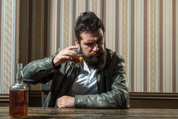 Fototapeta premium Man with beard holds glass brandy. Man holding a glass of whisky. Handsome stylish bearded man is drinking at home after work. Macho drinking. Degustation, tasting.