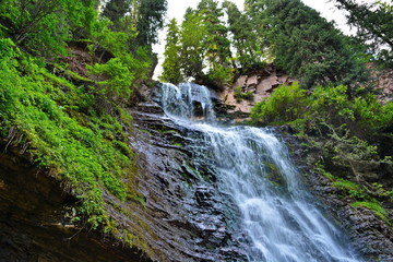 Top of the waterfall on a rock among trees and grass. Bottom view