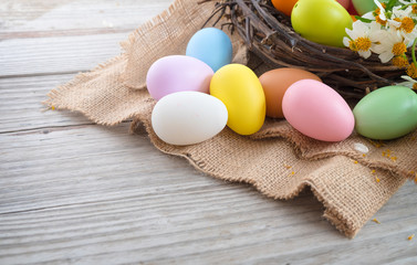 Fototapeta na wymiar Colorful Easter eggs in nest with flower on rustic wooden planks background. Holiday in spring season. vintage pastel color tone. Close up composition.