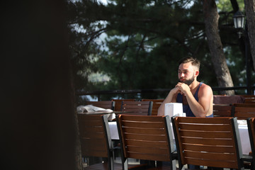 Young man with black hair and beard sitting in a restaurant in the Park in a summer evening