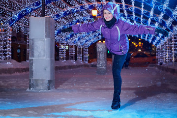 Girl skating on the ice arena in the evening city square in winter