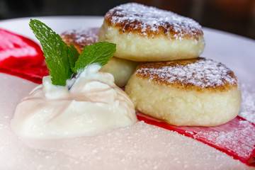 Traditional Russian sweet fried cheese cakes elegantly served on a plate with sour cream and jam, sprinkled with sugar in Russia