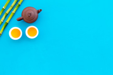 Asian tea traditions. Drink tea. Tea ceremony. Tea pot near cups of green tea and bamboo decoration on blue background top view copy space