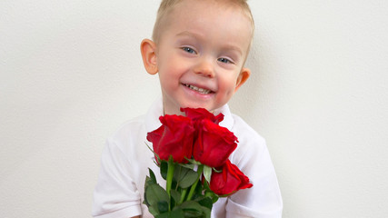 Cute kid ( two years old child)  holding the bouquet of red roses, smiling and looking at camera. Congratulations mother, womens, valentines day concept