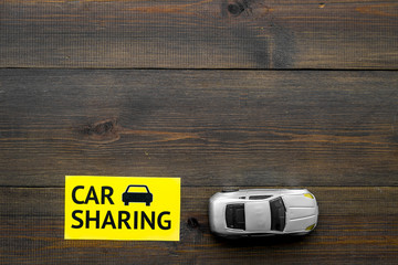Carsharing concept. Toy car near text car sharing on dark wooden background top view copy space