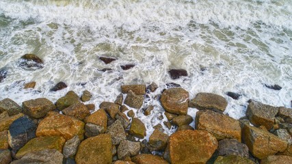 Top view of wave from the sea with fluffy white bubble which is coming and reaching brown beach rock