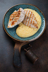 Plate with polenta and roasted chicken breasts, vertical shot on a dark brown metal background