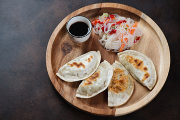Round wooden serving tray with pan fried korean potstickers, studio shot on a dark brown metal background
