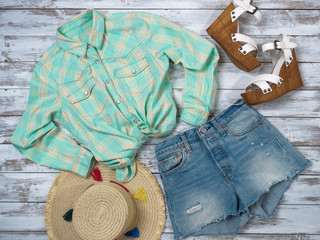 Womens clothing, accessories, shoes (plaid shirt, denim shorts, straw hat, wedge sandals). Fashion outfit, spring summer collection. Shopping concept. Flat lay, top down view